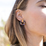 A close-up of a woman wearing Minimalist Circle Stud Earrings crafted from hypoallergenic materials, featuring a large, circular, multicolored gemstone with a gold accent, shown from the side against a blurred outdoor background.