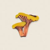 A handcrafted Chanterelle Mushroom Pin, shaped like two golden chanterelles with yellow tops and brown stems, displayed on a plain light background—an eco-friendly accessory for nature lovers.