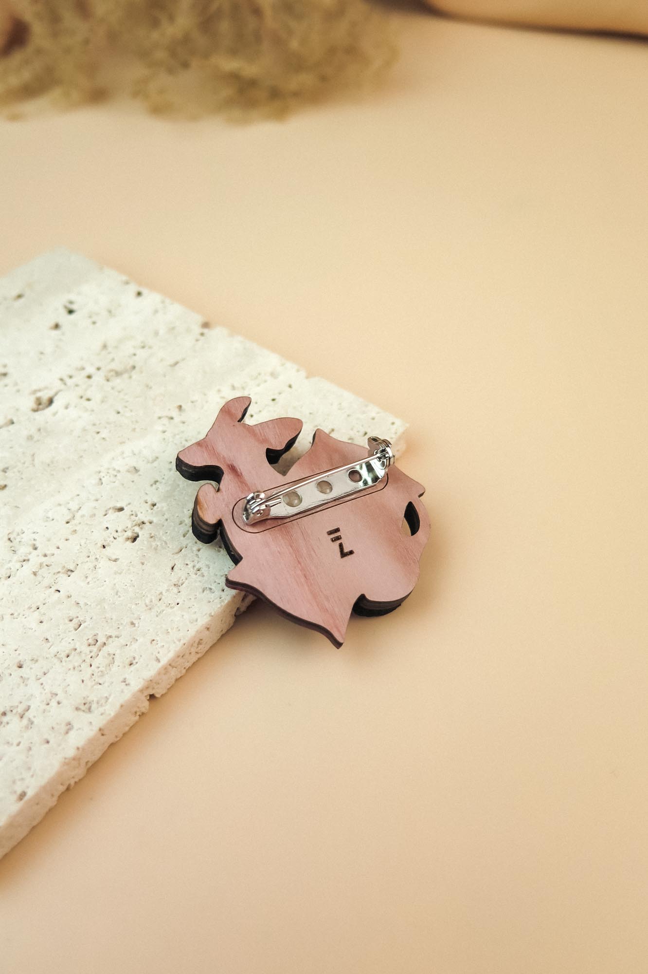A pink, animal-shaped dog pin with a silver clasp lies on a textured, off-white stone surface against a soft beige background—perfect for lovers of playful jewelry.