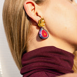 Woman with straight blonde hair wears a sleeveless maroon turtleneck and a colorful statement earring shaped like a halved fig with a gold mirror leaf accent. She is shown from the side, head slightly tilted back, highlighting the unique Fig Earrings and their handcrafted elegance.