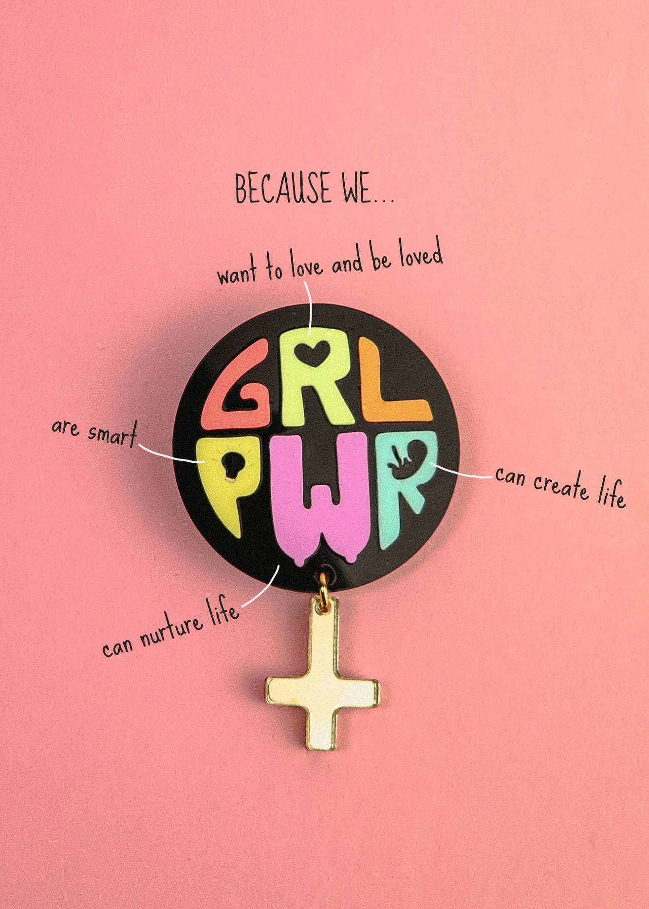 A colorful Girl Power Brooch reading GRL PWR is pinned to a pink background. Text around it says: Because we... want to love and be loved, are smart, can nurture life, can create life, with lines pointing to the badge.