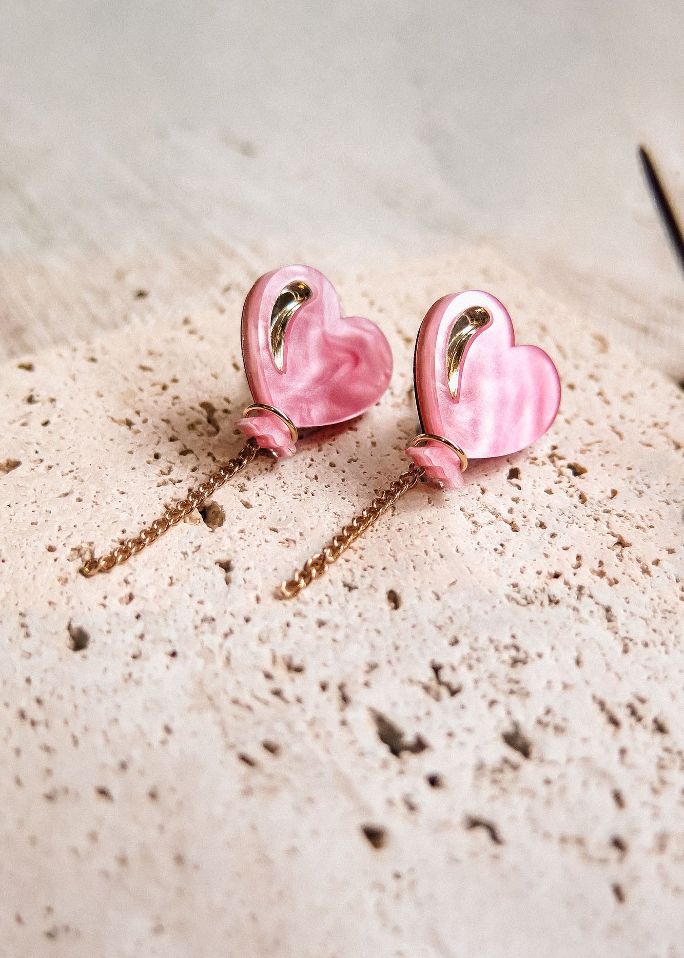 A pair of pink Heart Balloon Studs with gold accents and dangling gold chains, displayed on a textured, light-colored surface—perfect for adding vibrant style to any look.