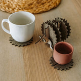 A white mug and a pink cup sit on spiky felt coasters shaped like a hedgehog, adding playful home decor flair to a light wooden table with a woven placemat in the background.