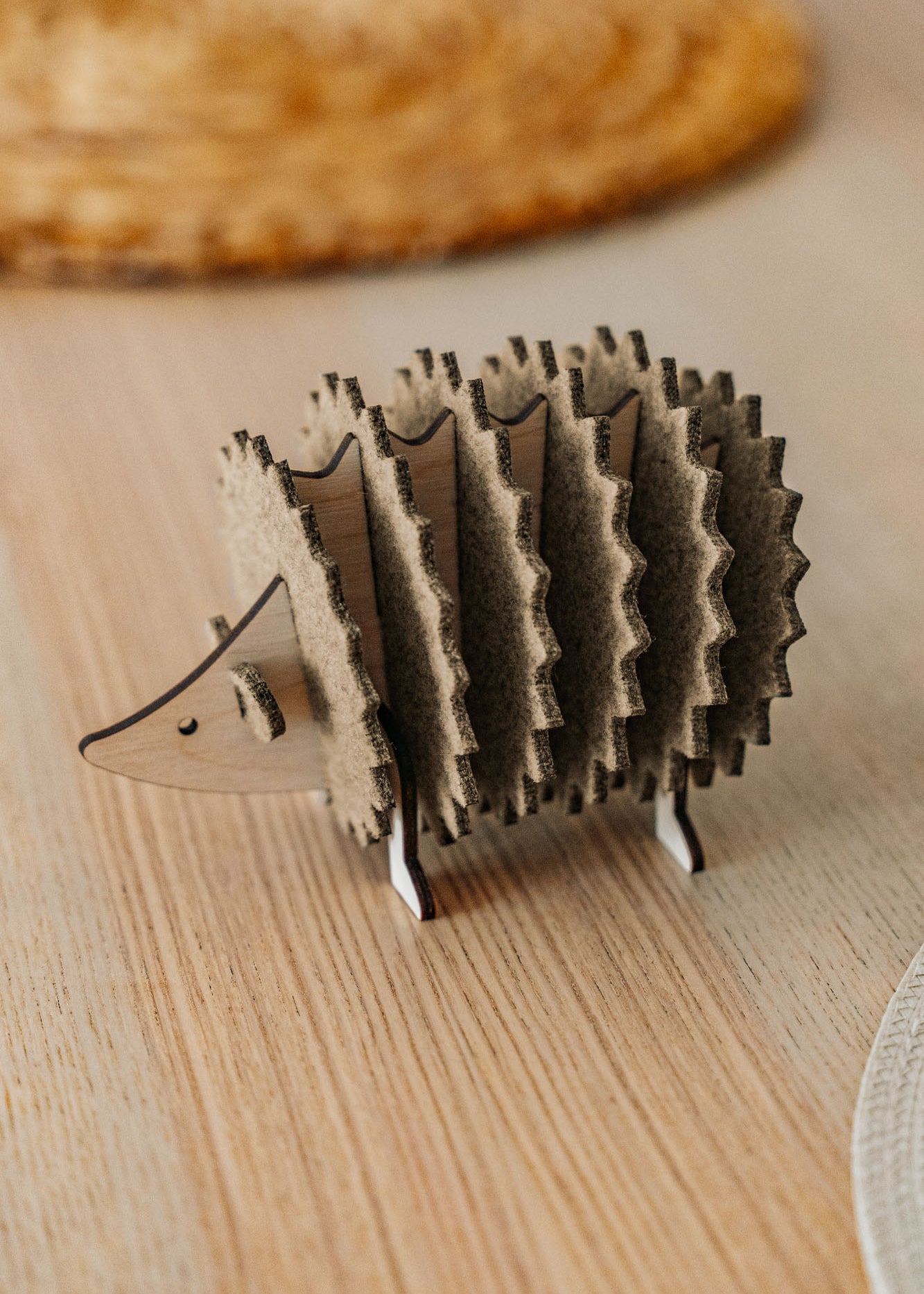 A small, wooden hedgehog-shaped coaster holder made of wood and felt sits on a light wooden table with a woven placemat in the background, adding a charming touch to your home decor.