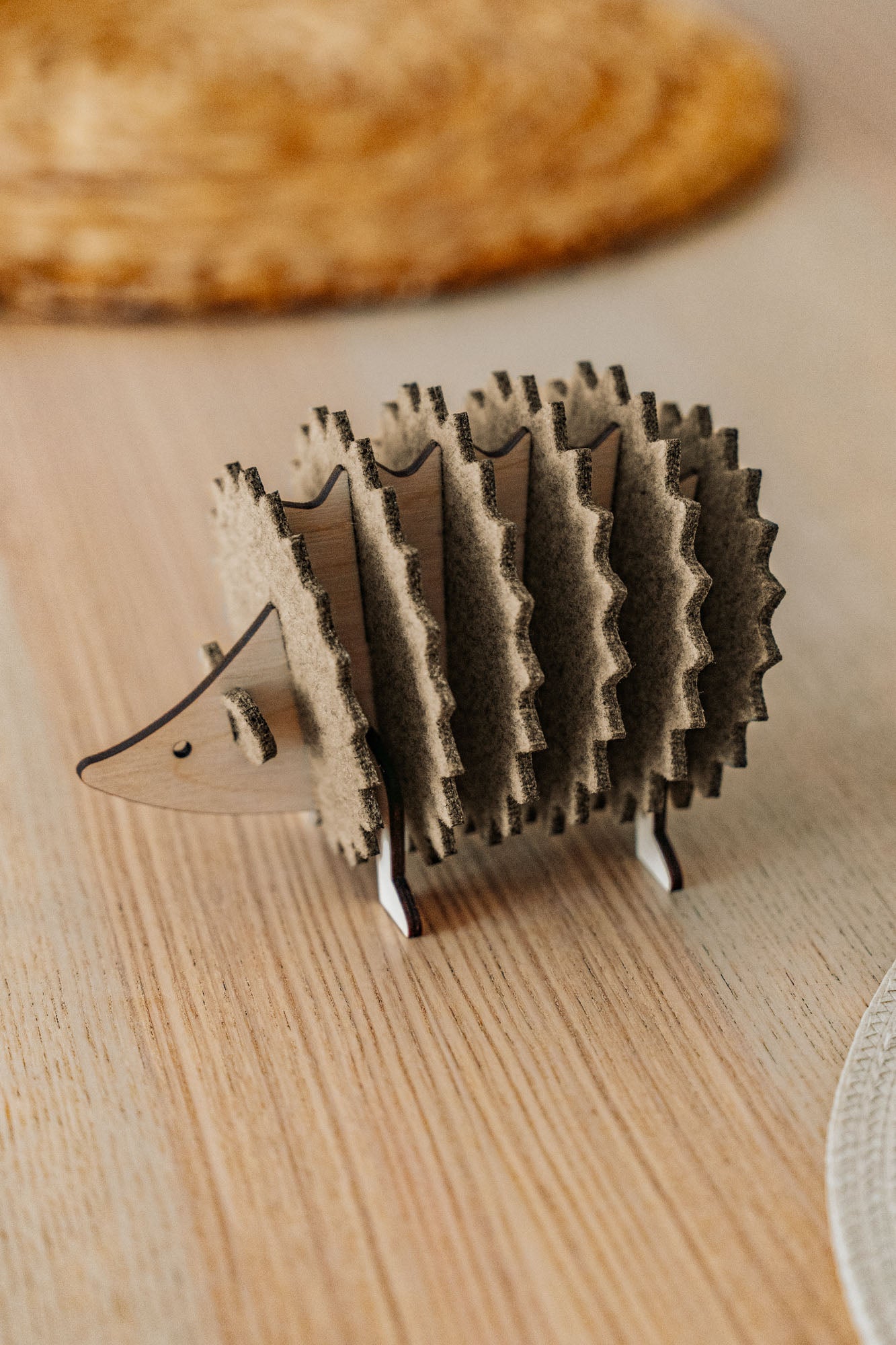 A small, wooden hedgehog-shaped coaster holder made of wood and felt sits on a light wooden table with a woven placemat in the background, adding a charming touch to your home decor.