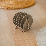 A small, decorative wooden hedgehog coaster holder made of felt and plywood sits on a wooden table, adding charm to your home decor, with woven placemats in the background.