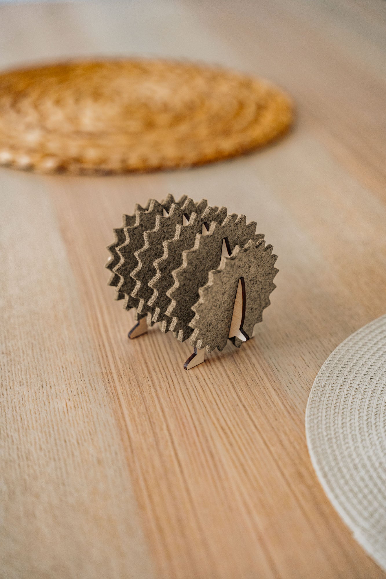 A small, decorative wooden hedgehog coaster holder made of felt and plywood sits on a wooden table, adding charm to your home decor, with woven placemats in the background.