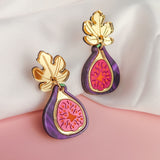 Handcrafted Fig Earrings shaped like figs with gold mirror leaves, featuring purple, pink, and gold details, displayed on a white and pink fabric background.