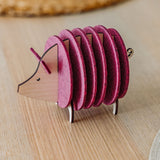 A small, decorative, pink and wood-colored armadillo figurine with a segmented, accordion-like body stands on a light wooden surface—perfect as a quirky housewarming gift.