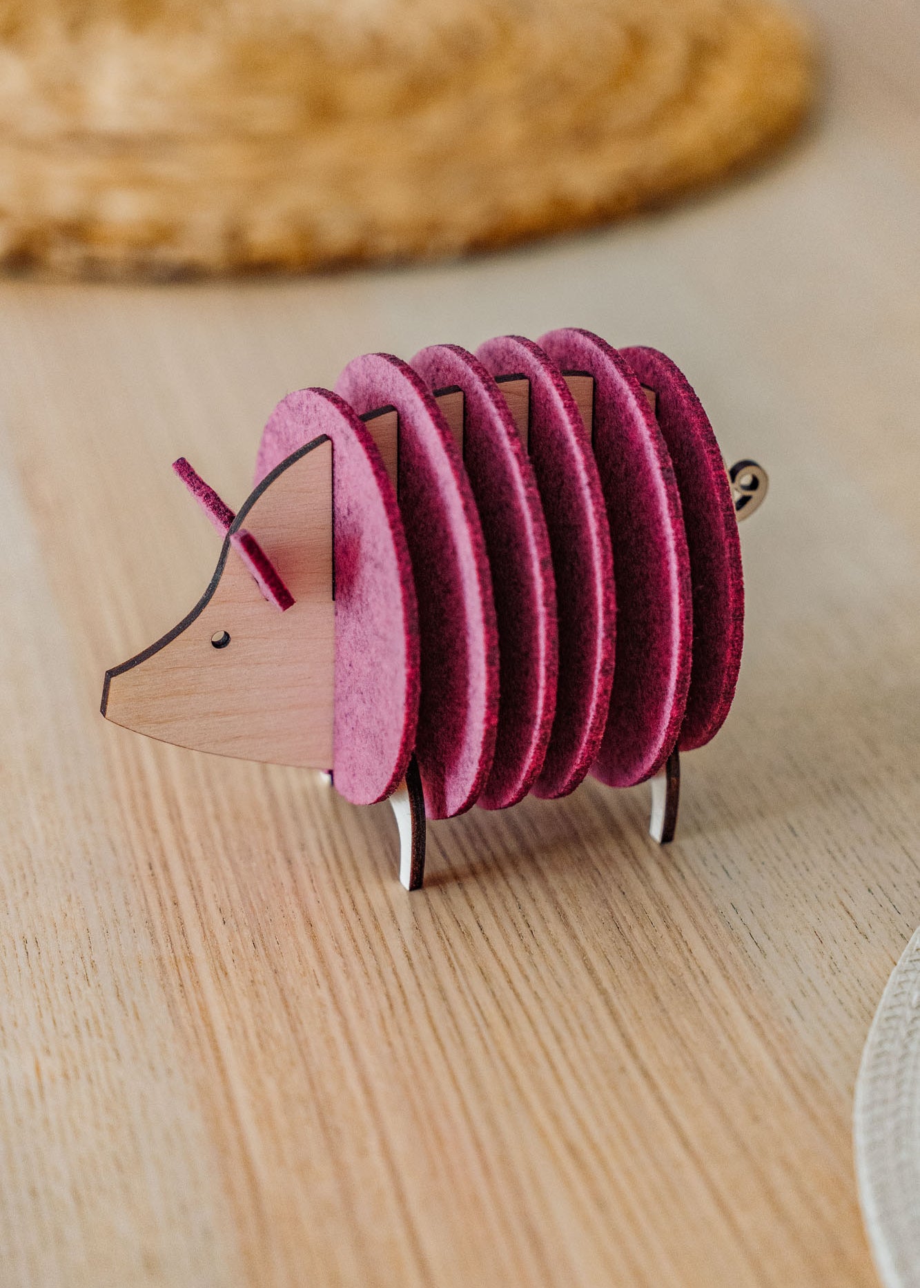A small, decorative, pink and wood-colored armadillo figurine with a segmented, accordion-like body stands on a light wooden surface—perfect as a quirky housewarming gift.