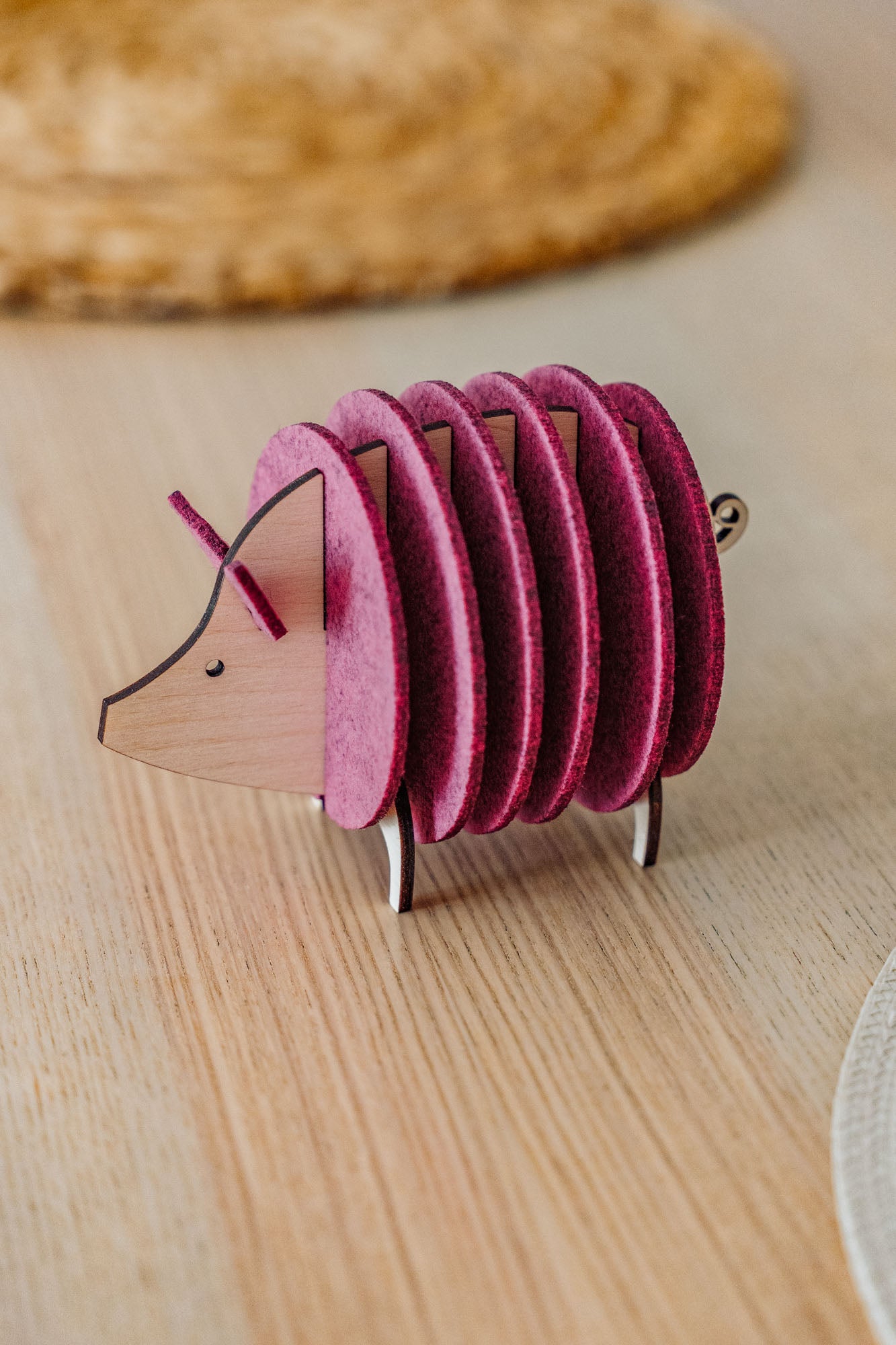 A small, decorative, pink and wood-colored armadillo figurine with a segmented, accordion-like body stands on a light wooden surface—perfect as a quirky housewarming gift.