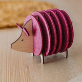 A wooden and felt coaster holder shaped like a hedgehog, with pink felt discs forming the body, sits on a light wooden table—a charming housewarming gift for any home.