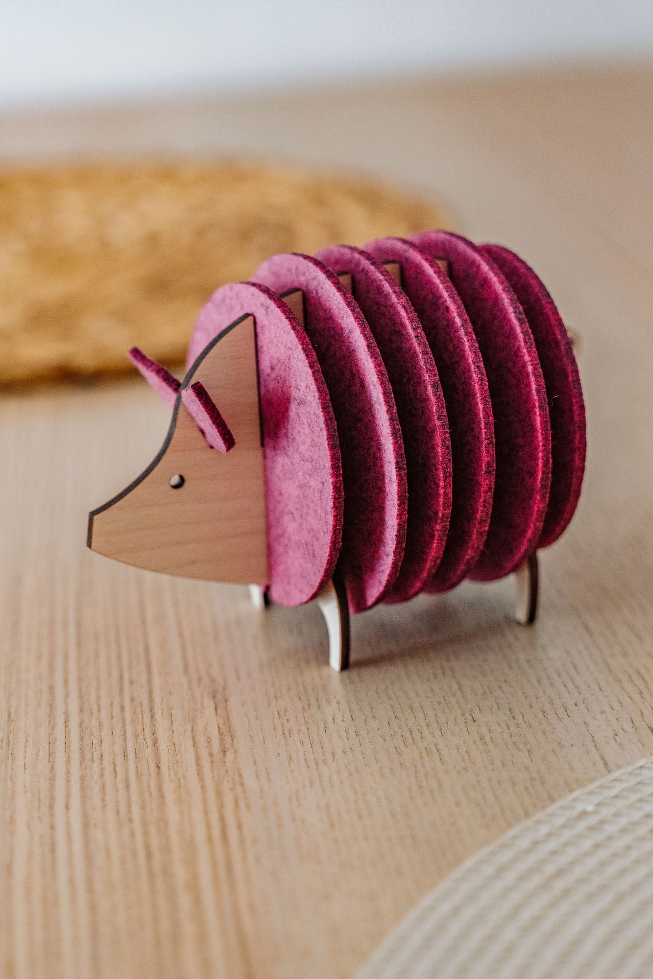 A wooden and felt coaster holder shaped like a hedgehog, with pink felt discs forming the body, sits on a light wooden table—a charming housewarming gift for any home.