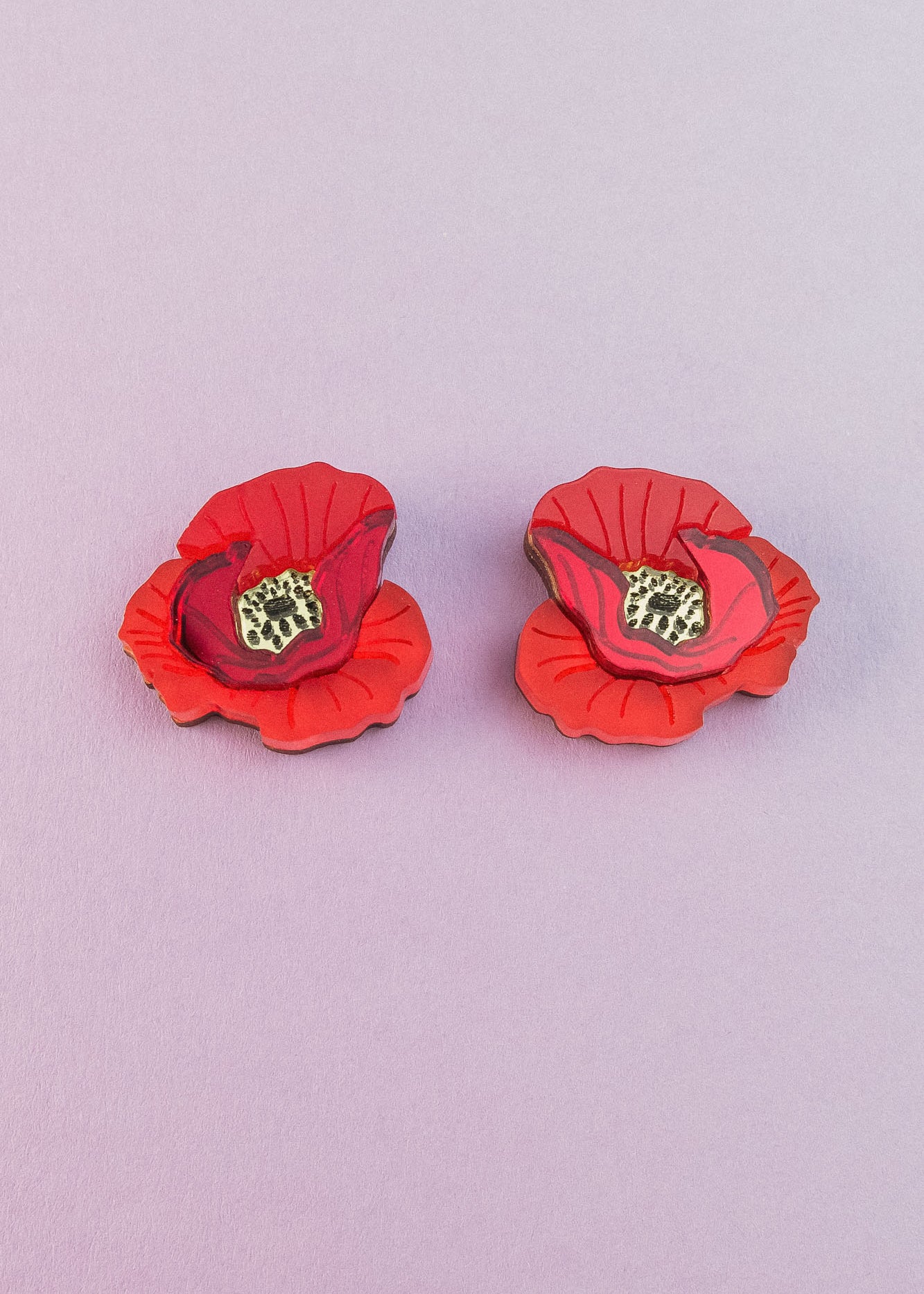 Two lightweight acrylic earrings featuring a vibrant poppy design with black and yellow centers are displayed on a light purple background.