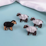 Four geometric sheep figurines on a light blue surface—three are white with brown accents, and one is black with tan accents. A white cloth is in the background, perfect for animal lovers seeking unique decor or a Sheep Badge-inspired accent.