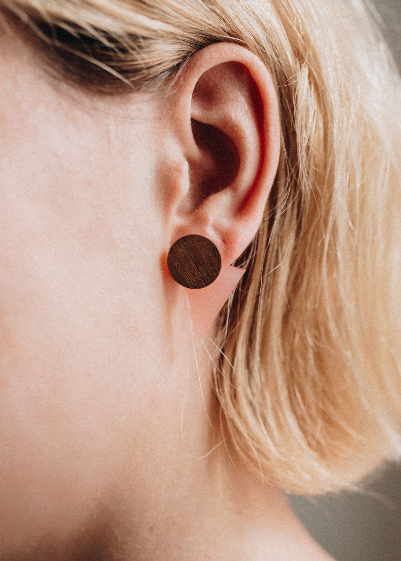 Close-up of a person with short, blonde hair wearing a large, round, handcrafted wooden stud earring in their ear. The focus is on the ear and earring, perfect for elevating any contemporary capsule wardrobe.