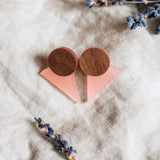 A pair of handcrafted triangle earrings featuring round wooden tops and pink triangular bases are displayed on beige linen fabric, with dried lavender sprigs nearby—perfect for a contemporary capsule wardrobe.