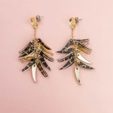 A pair of featherlight dangle earrings with layered gold and tortoiseshell-patterned pieces arranged in a fan-like design, displayed on a light pink background.
