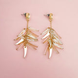 A pair of gold and clear featherlight dangle earrings with multiple dangling, leaf-shaped charms arranged in layered clusters, displayed on a soft pink background.
