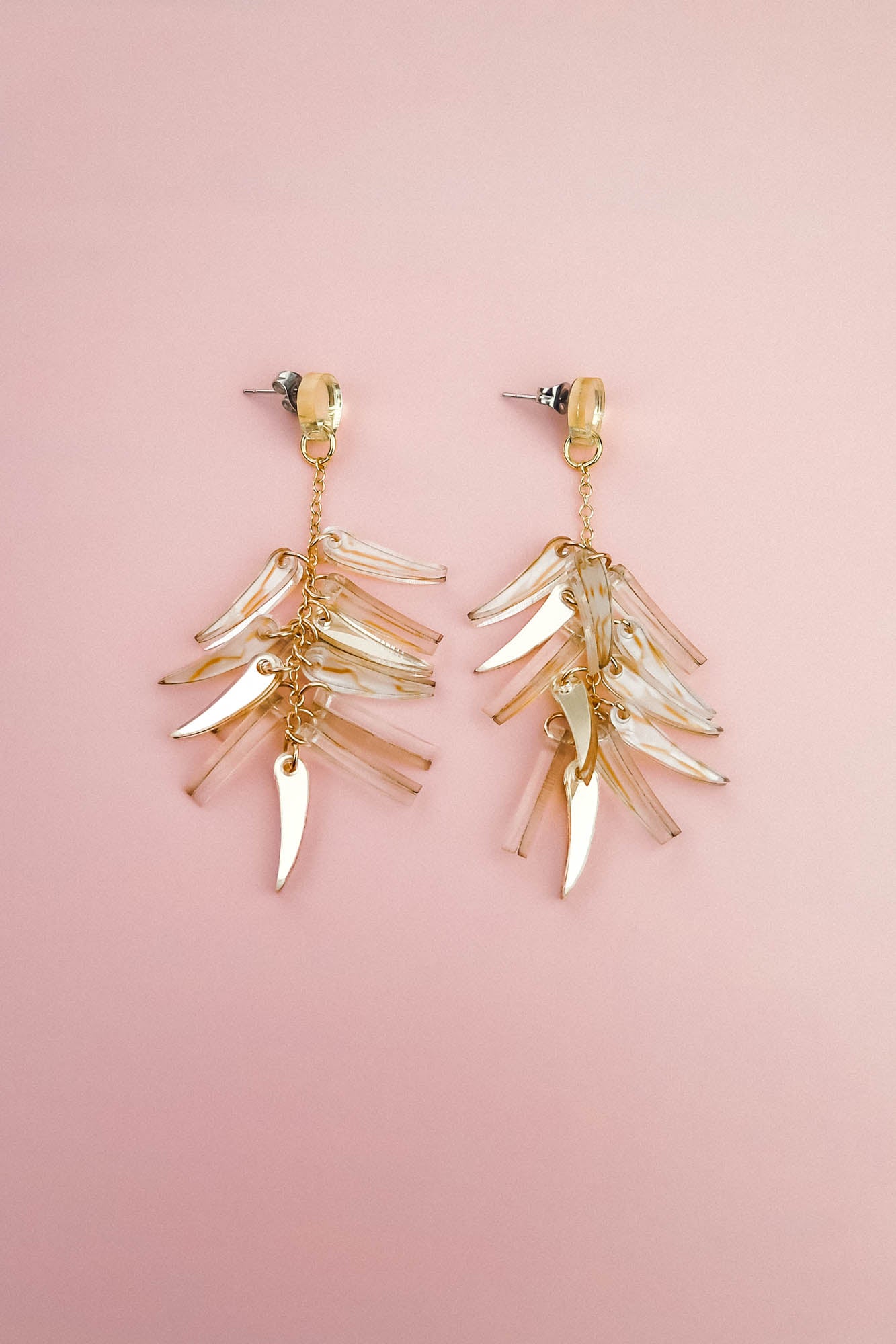 A pair of gold and clear featherlight dangle earrings with multiple dangling, leaf-shaped charms arranged in layered clusters, displayed on a soft pink background.
